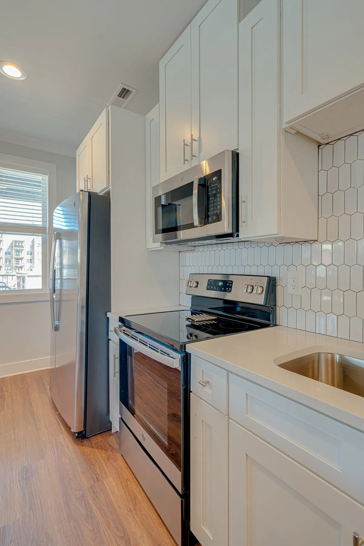 A bright, modern kitchen with stainless steel appliances, white cabinetry, a striking hexagonal backsplash, and a spacious countertop. The space is uncluttered and functional, showcasing everything a guest needs for cooking, entertaining, or simply enjoying a morning coffee.