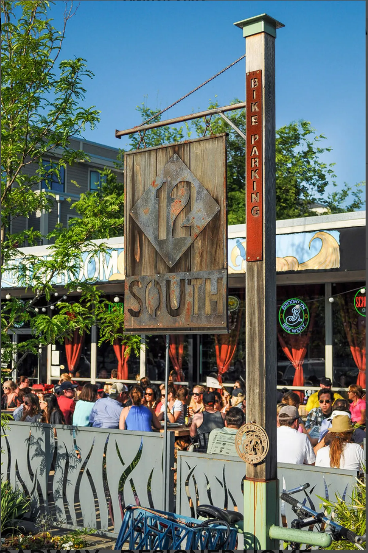 A bustling outdoor dining scene with the '12 South' sign, bike parking, a decorative fence, and patrons enjoying food and drinks. The image highlights social interaction and the vibrant culinary culture present in Nashville's trendy neighborhoods.
