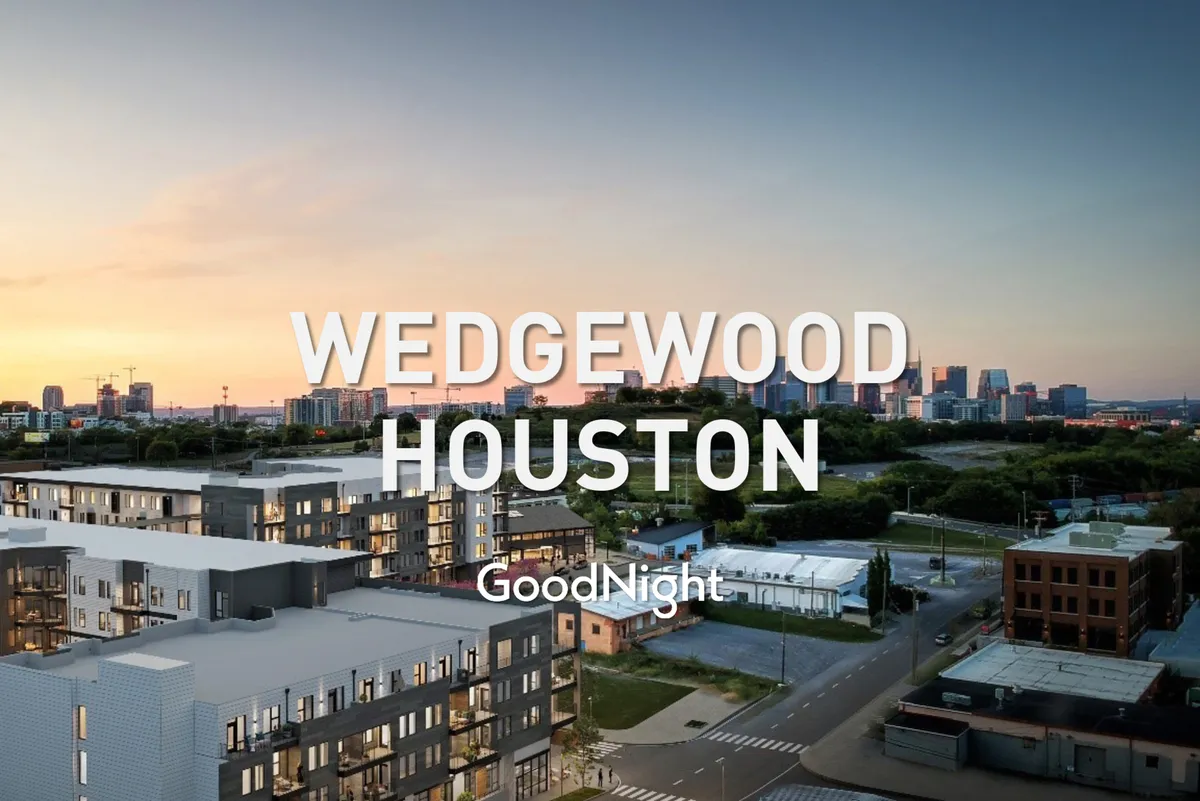 A view of modern residential buildings set against the Nashville city skyline, with a warm sunset sky overhead. The scene captures an inviting, urban neighborhood atmosphere, suggesting proximity to city conveniences and vibrant local life.