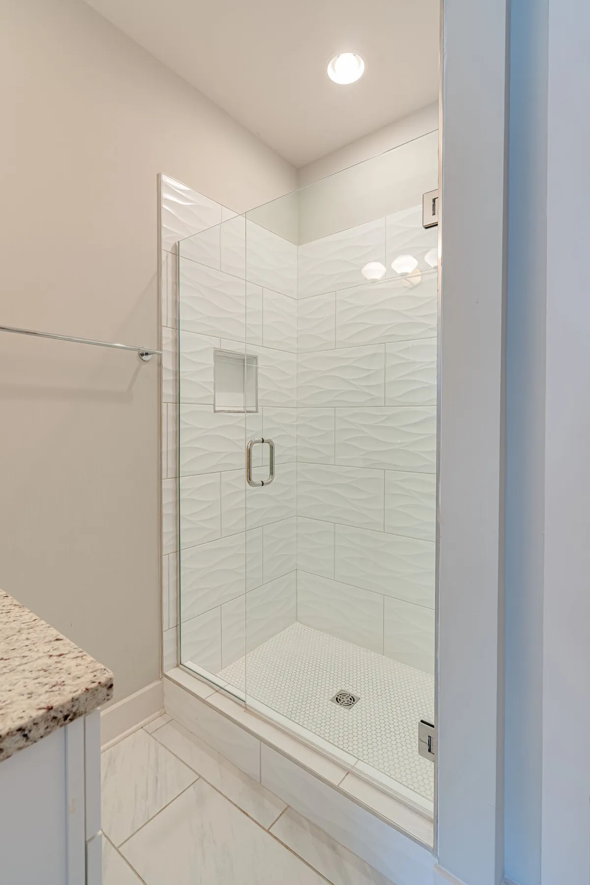 A contemporary bathroom showcasing a glass shower enclosure, textured wall tiles, and a granite countertop. The space is clean, stylish, and gives off a spa-like, refreshing vibe.
