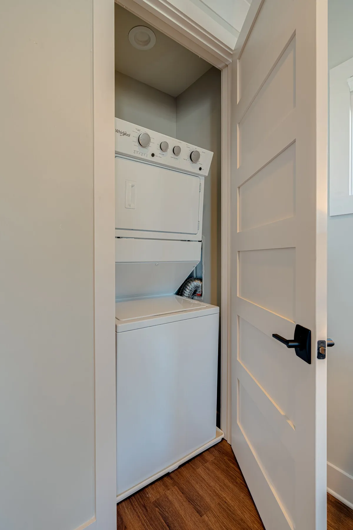 A neat laundry area with a stacked washer and dryer, white cabinetry for storage, and a wooden floor. The room is functional and organized, underscoring the ease and convenience of home-like amenities.