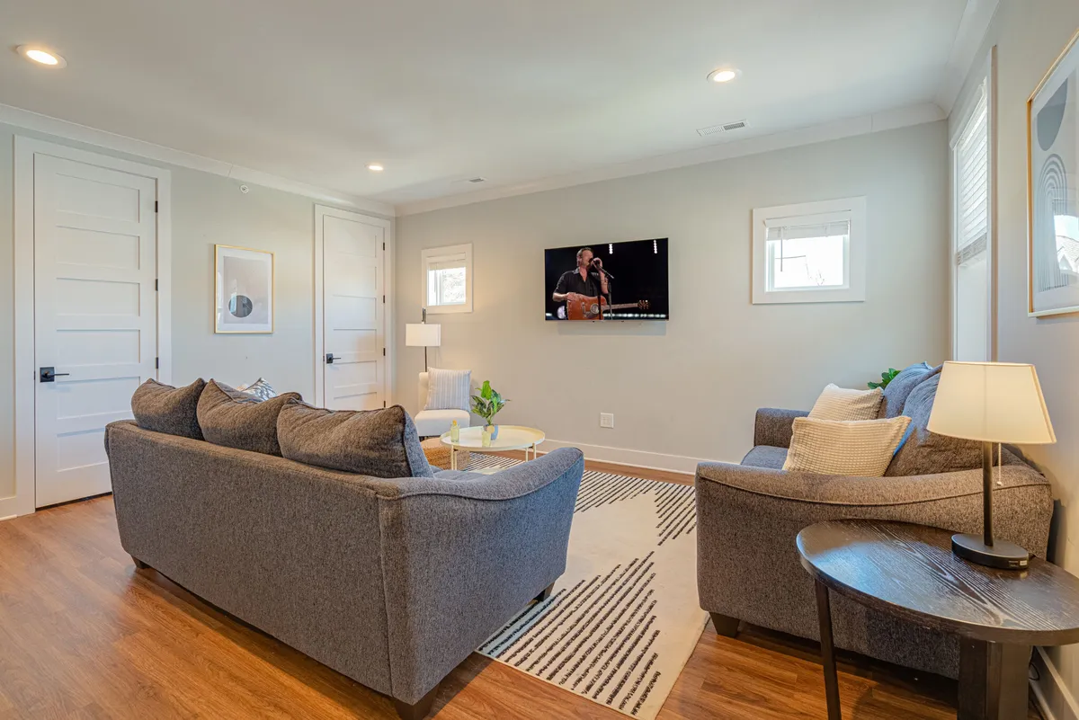 A cozy open-concept living room with comfortable gray sofas arranged around a modern coffee table, a large television mounted on the wall, and stylish decor. The inviting seating arrangement encourages relaxing, socializing, or enjoying a movie night. The space feels airy and welcoming, ideal for both quiet downtime and gatherings.